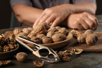 Elderly woman with nutcracker, whole and peeled walnuts at wooden table