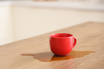 Red cup and spilled coffee on table in kitchen, closeup