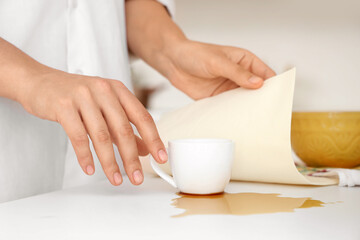 Woman wiping spilled coffee on counter in kitchen, closeup