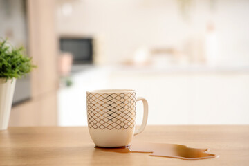 Cup and spilled coffee on table in kitchen, closeup