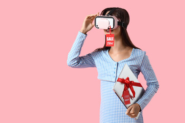 Young woman in VR glasses with laptop on pink background. Cyber Monday