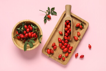 Wooden tray and bowl with fresh rose hip berries on pink background