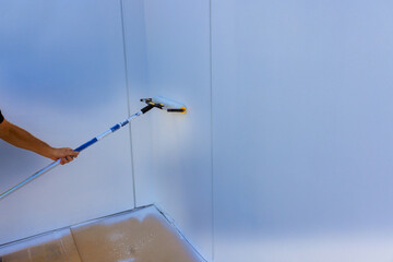 Obraz premium Handyman is using paint roller on wall in bright room, focusing on even coverage.