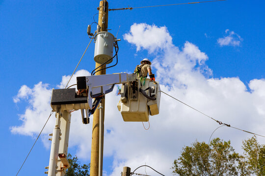 Utility electrical worker in bucket lifts to repair power lines on tall wooden pole under works day