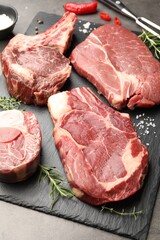 Pieces of raw beef meat, spices and carving fork on grey table, closeup