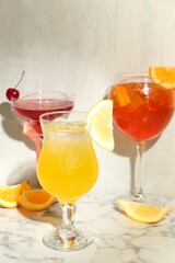 Glasses of tasty cocktails with garnish on white marble table, closeup