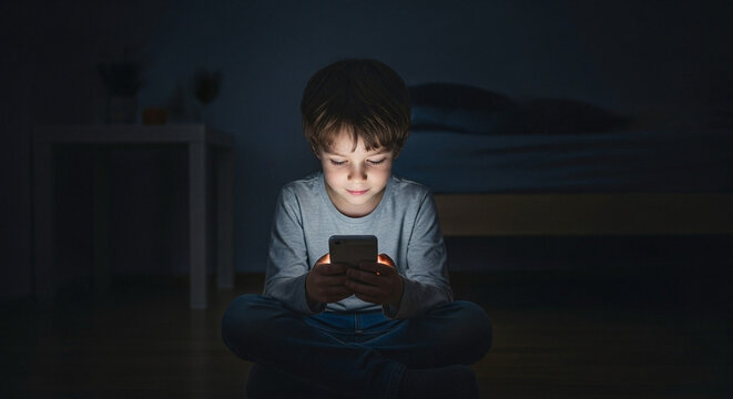 ''A young boy sits cross-legged in a dimly lit room, illuminated by the soft glow of his smartphone, creating an atmosphere of ...