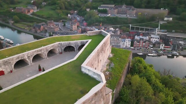 citadel mountain top church below green cover town meuse river train parked tracks dinant belgium diverse to left right circling aerial shot 