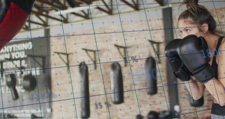 Standing woman in sportswear punching red bag with boxing gloves at gym, grid overlay, copy space