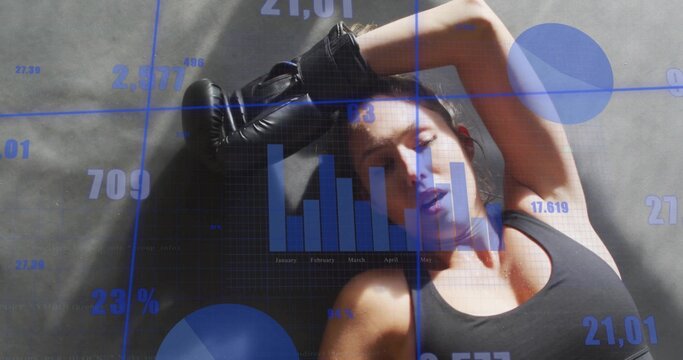 Resting athlete lying on dark mat in gym, wearing black sports bra, gloves, blue data overlays - Powered by Adobe