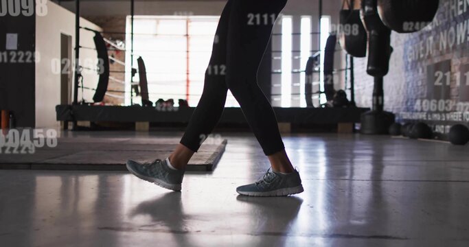 Fototapeta Walking gym goer wearing black leggings and gray trainers in gym training room, with punching bags