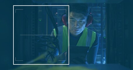 Kneeling Korean technician inspecting tablet in data center, with LEDs server racks safety vest