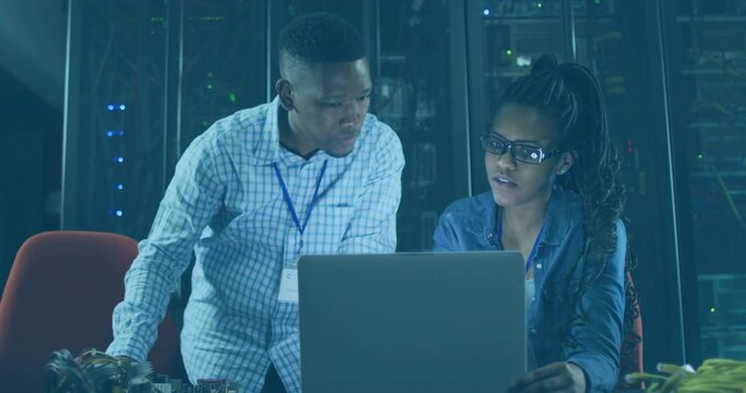 Two IT professionals troubleshooting network equipment in data center, with laptop, server racks