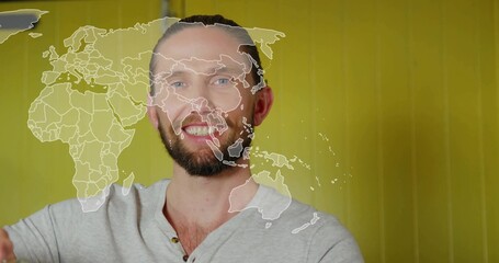 Smiling male presenter in grey henley shirt sharing global trends in studio, with world map overlay