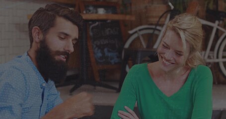 Talking bearded man with listening woman in green top at cafe, with chalkboard menu, bicycle