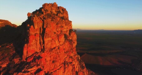Towering red sandstone cliff glowing with warm light on desert plateau, sparse shrubs, copy space