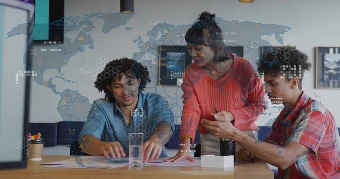 Collaborating team analyzing charts at office desk with water glass, tumbler, supplies, map overlay