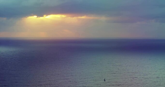 Fototapeta Small sailboat silhouette drifting in open sea, with sunlight beams piercing clouds, copy space