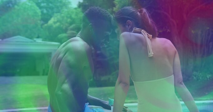 Chatting man in swim trunks and woman in halter swimsuit at suburban backyard pool, with smartphone