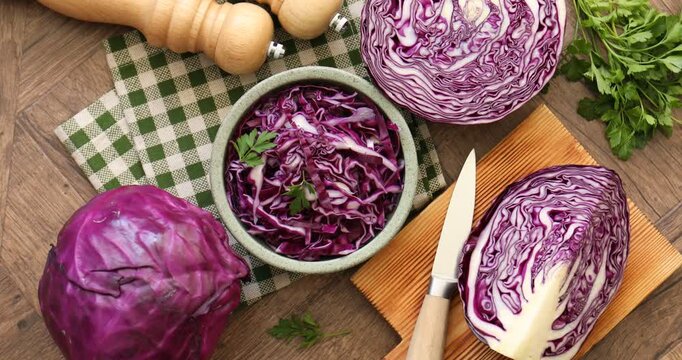Fresh red cabbages, parsley and knife on wooden table, flat lay. Camera spinning over