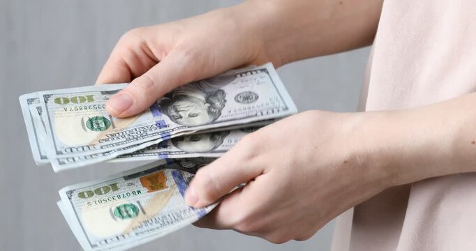 Alimony. Woman counting dollar banknotes on blurred background, closeup
