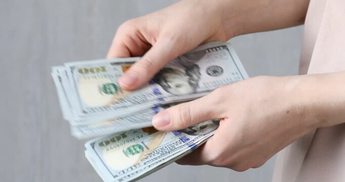 Alimony. Woman counting dollar banknotes on blurred background, closeup