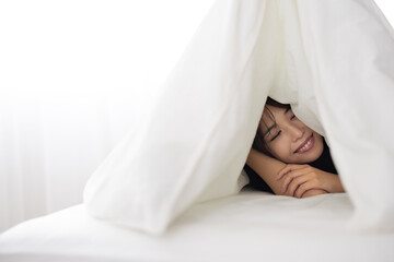 Young Woman Smiling Under Blanket on Bed in Bright Room