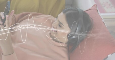 Mid-adult woman lying tapping smartphone streaming audio and activating tech waveform overlay - Powered by Adobe