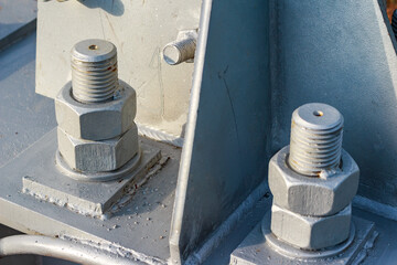 Close-up of heavy-duty metal bolts and nuts securing a structure, coated in grey paint. Industrial fastening detail highlighting strength and construction