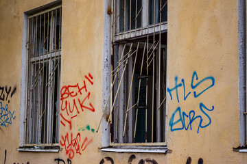 Grungy facade with two broken windows, twisted metal bars, and vivid graffiti on a cracked,...