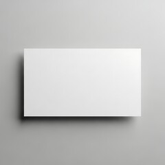 Fototapeta premium A blank, white rectangular card or paper sheet placed on a light gray surface, casting a soft shadow.