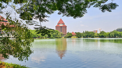 Obraz premium reflection of building on Kenanga Lake. Rectorate Building of the University of Indonesia. with trees as frame and blue sky