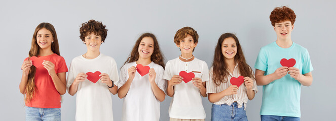 Happy smiling group of young school children friends holding paper red hearts in hands together...