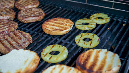 Grilled hamburger patties and pineapple slices on barbecue grill, with toasted burger buns, showcasing delicious outdoor cooking experience