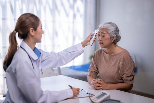Doctor taking senior asian woman's temperature at clinic checkup