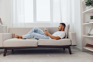 Relaxed man reading a book on a cozy sofa in a bright, modern living room. The natural light...