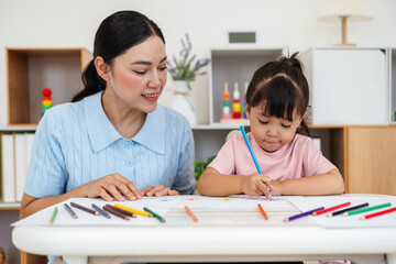 toddler baby girl training to drawing with colored pencil with mother helping on desk at home