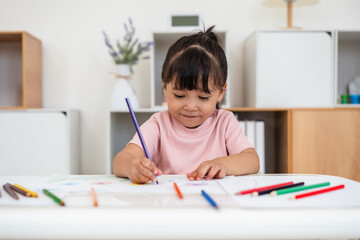 happy toddler baby girl training to drawing with colored pencil on desk at home