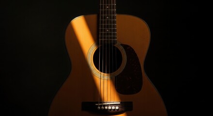 Fototapeta premium Acoustic guitar bathed in dramatic sunlight against a dark backdrop.