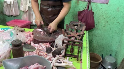 A local butcher is seen expertly preparing raw chicken, with various cuts and a pile of chicken feet, at a bustling traditional market stall, reflecting daily life and fresh meat trade.