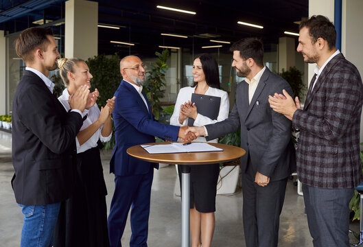 Handshake of business partners, applause of people on round table meeting in modern office. Executive managers shake hands, excited colleagues team clapping in support. Partnership, leadership concept