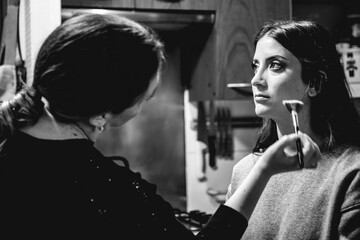 A make-up artist getting a beautiful and young brunette model ready for a photoshoot (in black and white)