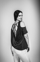 Fashion black and white portrait of a beautiful brunette woman smiling in a styling outfit on light gray studio background