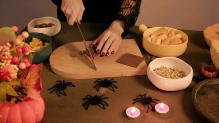 Woman chops chocolate bar on a wooden cutting board hands carefully slice pieces for baking festive cookies - Powered by Adobe
