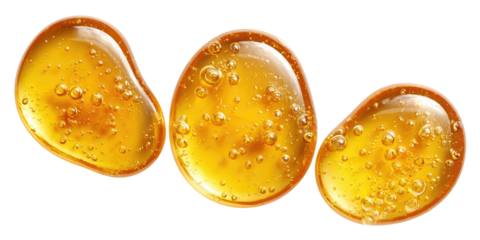 Three glistening golden honey drops or cosmetic oil beads with internal reflections