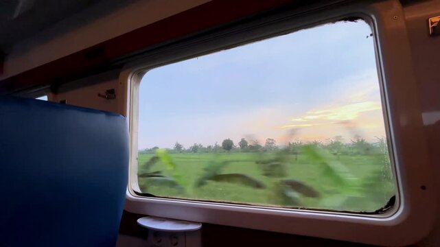View from the train window. Beautiful view from the window of a long-distance train, with green rice fields stretching out and residential areas on the edge of the rice fields during a light rain.
