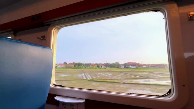 View from the train window. Beautiful view from the window of a long-distance train, with green rice fields stretching out and residential areas on the edge of the rice fields during a light rain.
