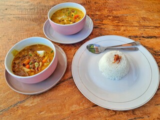 Richly flavored Beef Tongseng Curry and Sour-Sweet Beef Stew (Asem-Asem Sapi) served in bowls with white rice topped with fried shallots on a wooden table. An authentic warm meal.