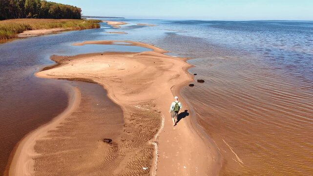 Tourist walking barefoot on a thin strip of sand connecting small islands in a river delta