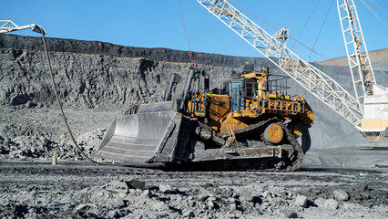 A huge crawler tractor bulldozer is cleaning and leveling excess excavation material in an open-pit...